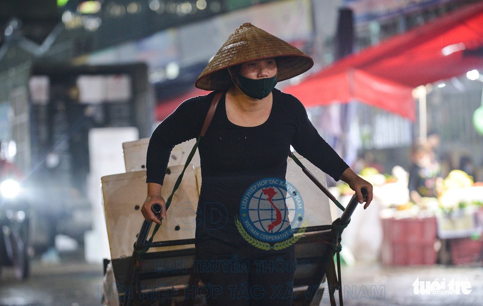 Một nữ cửu vạn gồng mình kéo xe hàng tại chợ Long Biên - Ảnh: TUỆ VĂN